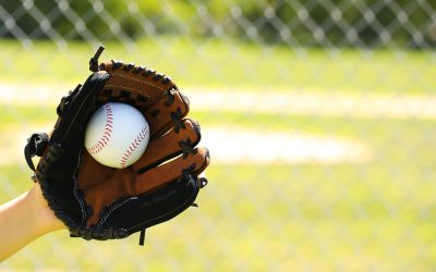 Hand of Baseball Player with Glove and Ball over Field and Net